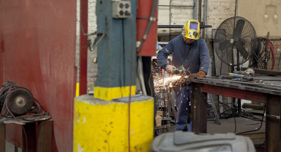 Factory worker uses grinding tool on metal tube at custom manufacturer in Chicago Heights Illinois